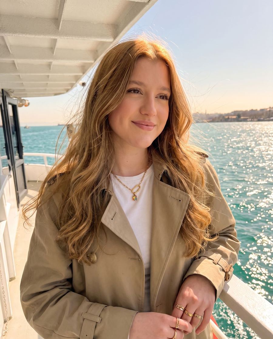 Leyna auf einer Fähre am Meer, lächelnd, mit goldener Kette und Ringen